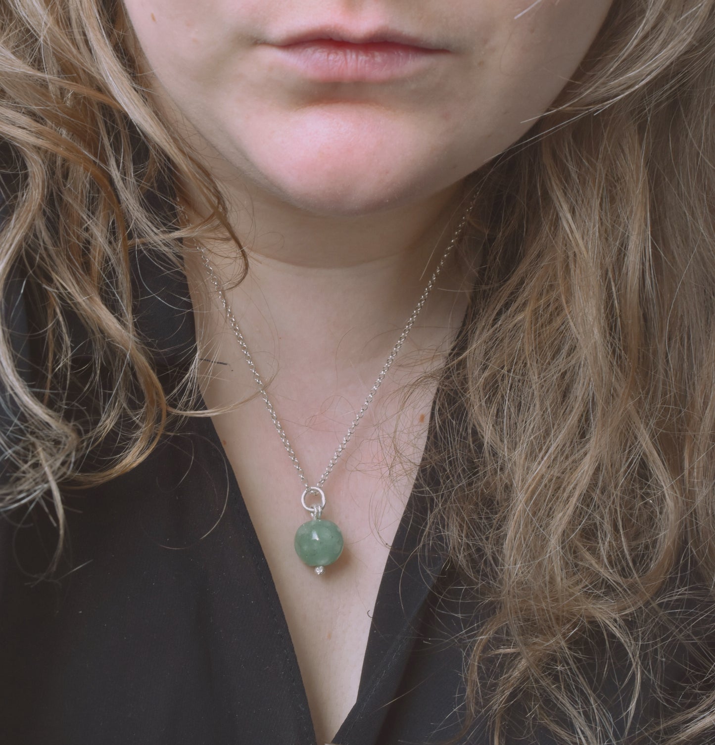 Carved aventurine silver pendant on a silver chain worn by a woman with long hair