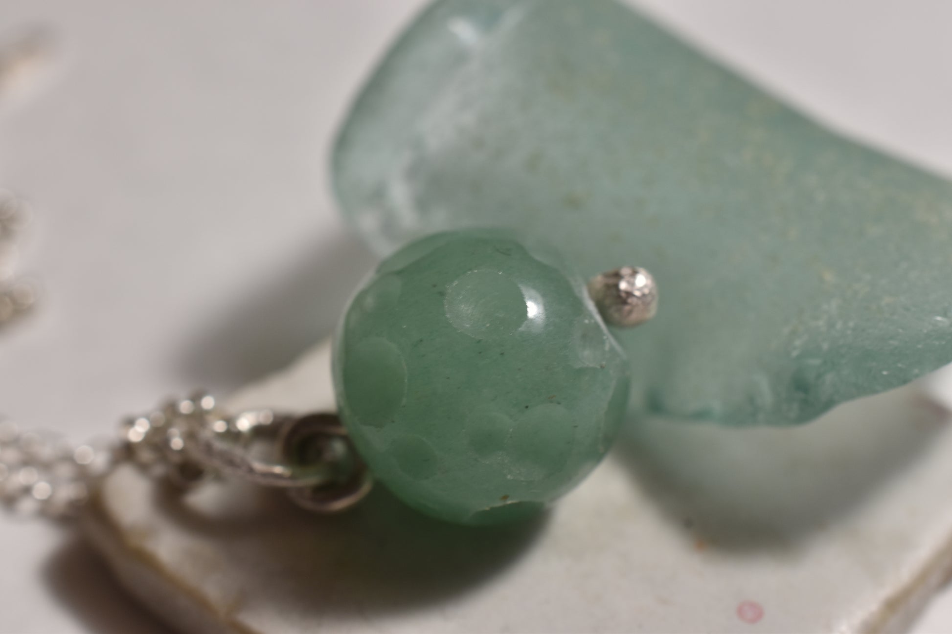 This image features a close-up view of a unique pendant named the "Crater Pendant." The pendant displays a large, spherical bead with a translucent green color, reminiscent of a marble or a crystal.