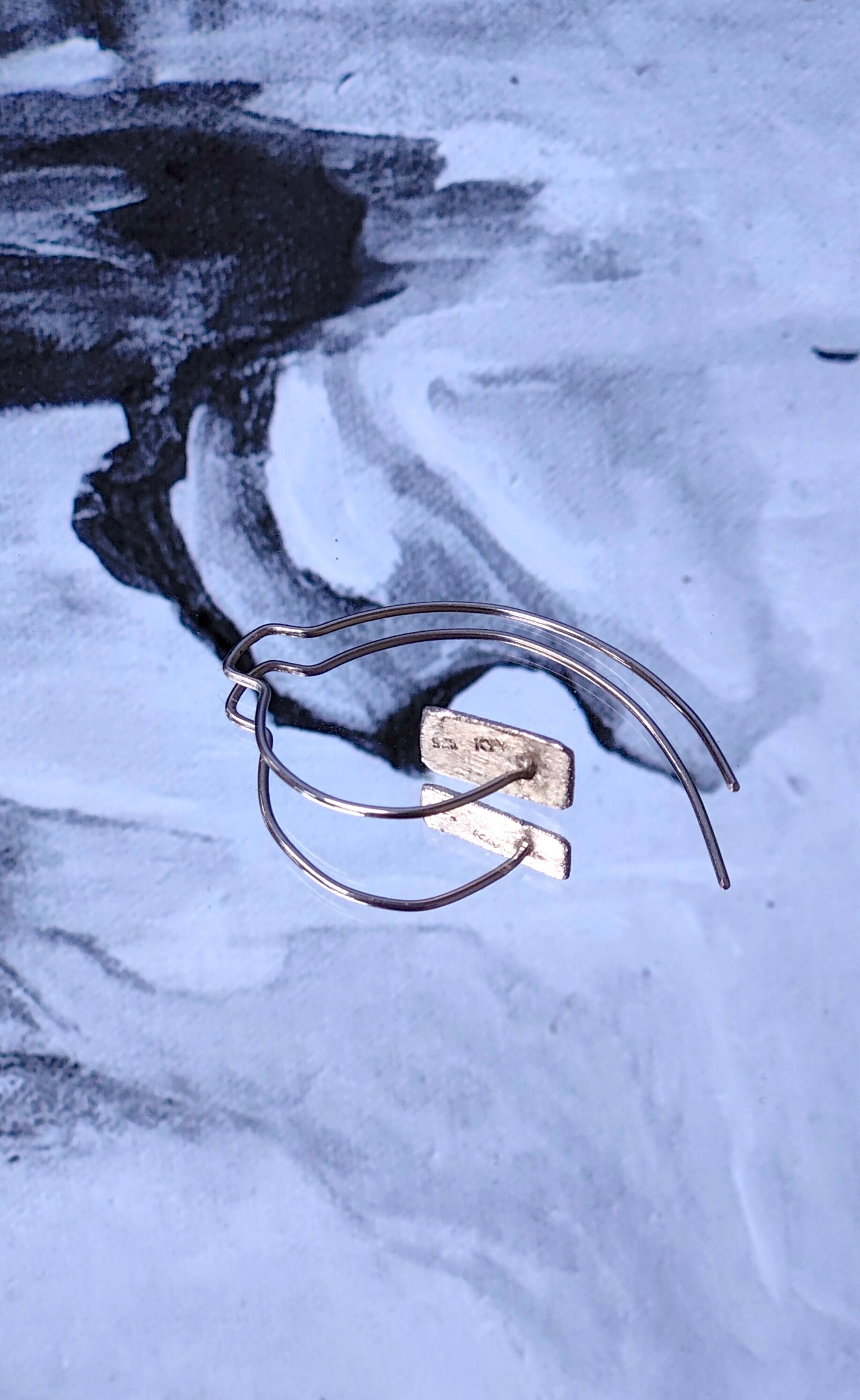 Silver spiral hoop earrings on a textured gray surface