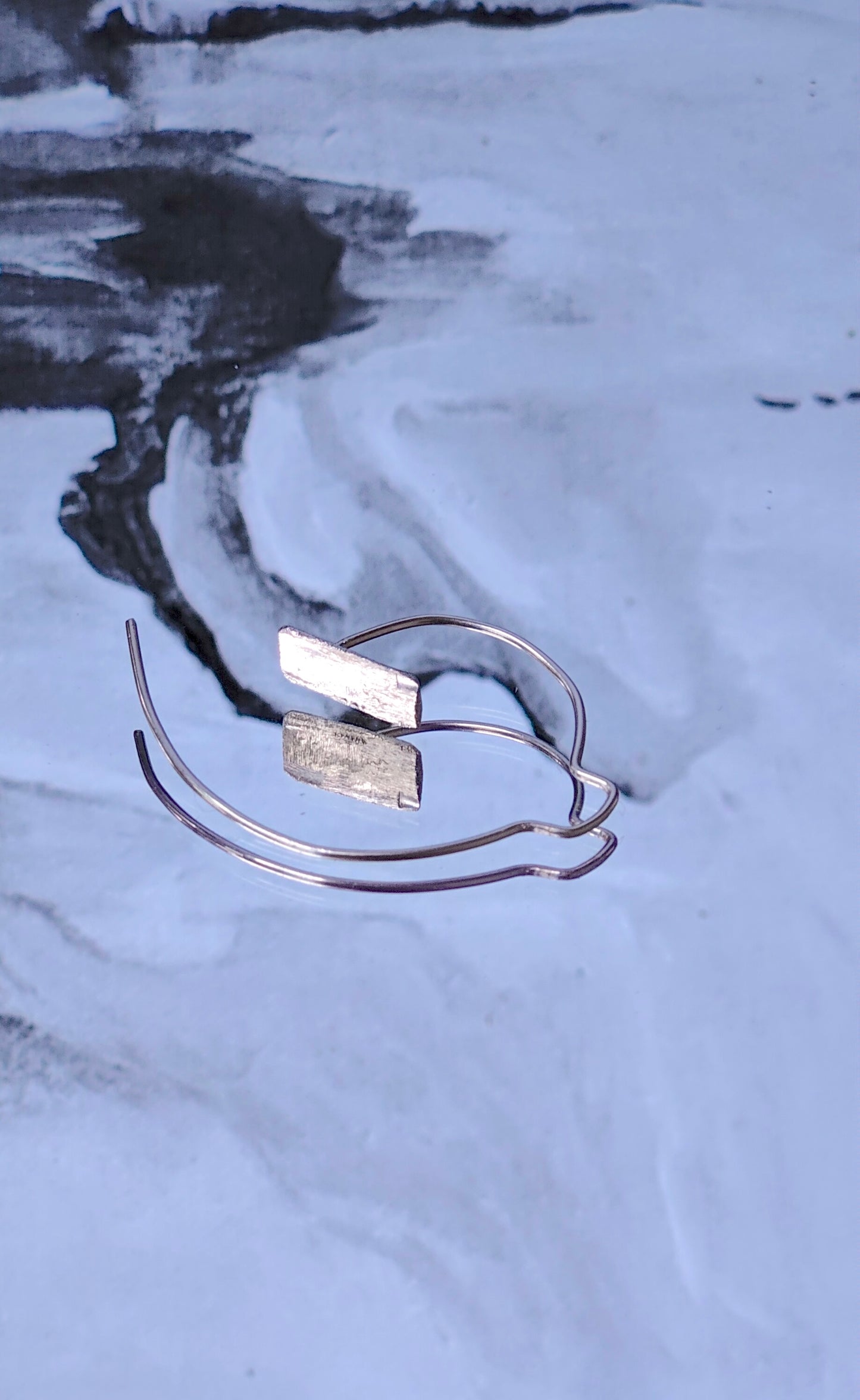 Handmade artisan sterling silver spiral hoop earrings on a textured gray surface